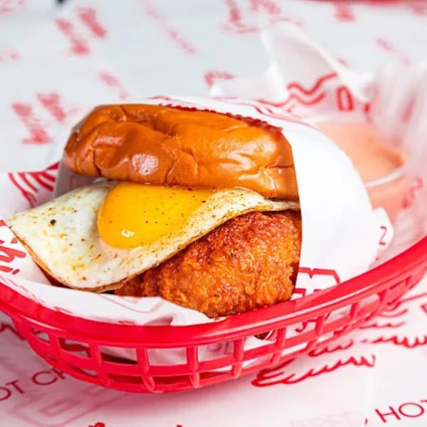 Bred Hot Chicken sandwich with fried chicken, fried egg, and sauce in a red basket.