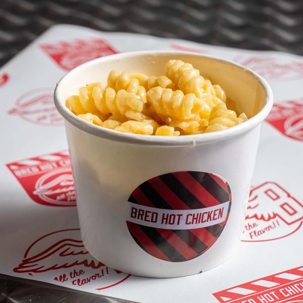 Mac and cheese in a white cup with the "Bred Hot Chicken" logo on a branded paper.