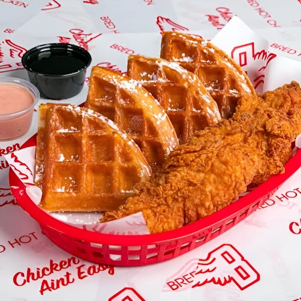 Bred Hot Chicken's fried chicken and waffles with powdered sugar, syrup, and dipping sauce.