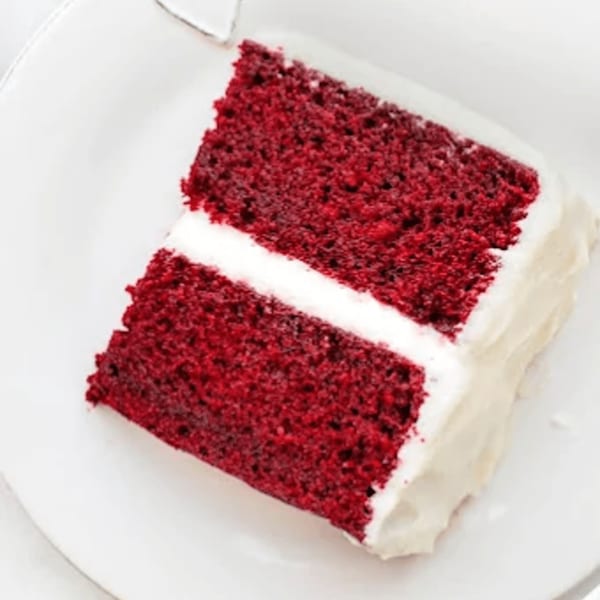 A slice of Bred Hot Chicken's red velvet cake with white frosting on a white plate.
