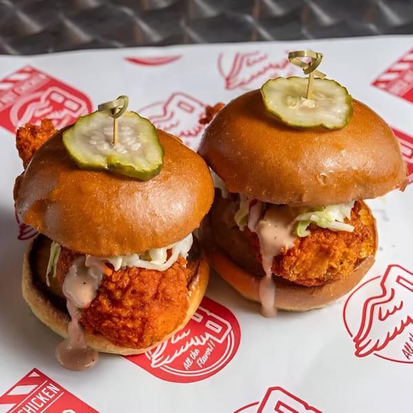 Two Bred Hot Chicken sliders with fried chicken, coleslaw, sauce, and a pickle on top.