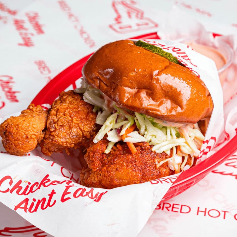 Bred Hot Chicken sandwich with coleslaw and pickles, alongside fried chicken pieces in a red basket.